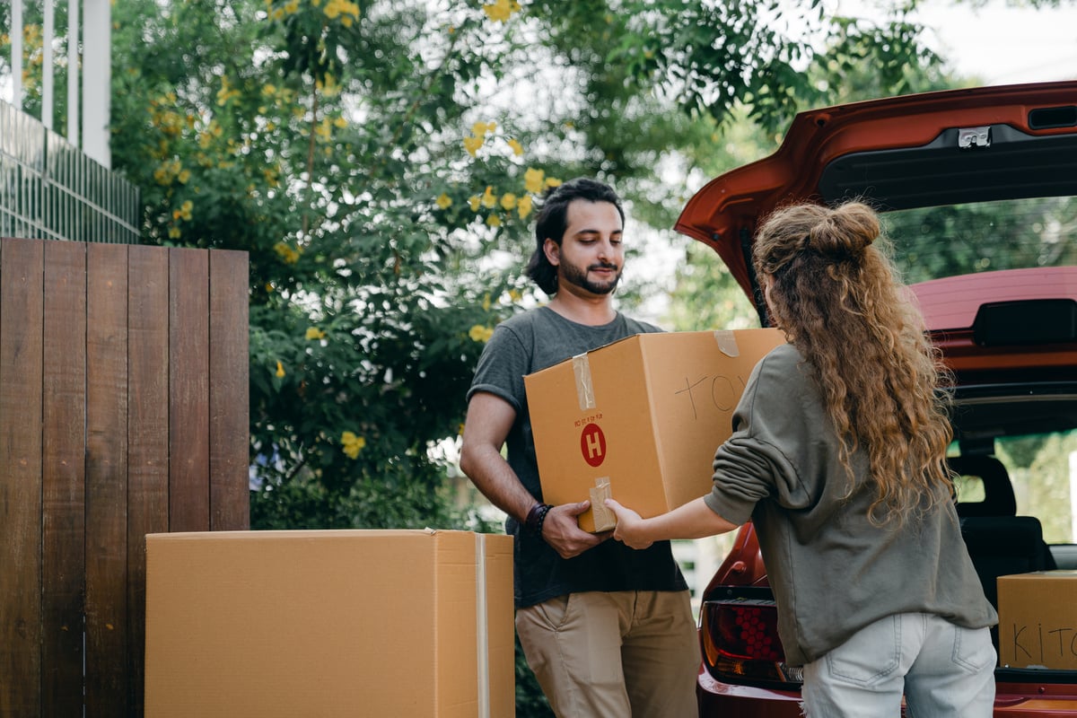 Couple passing carton box to each other while unpacking car